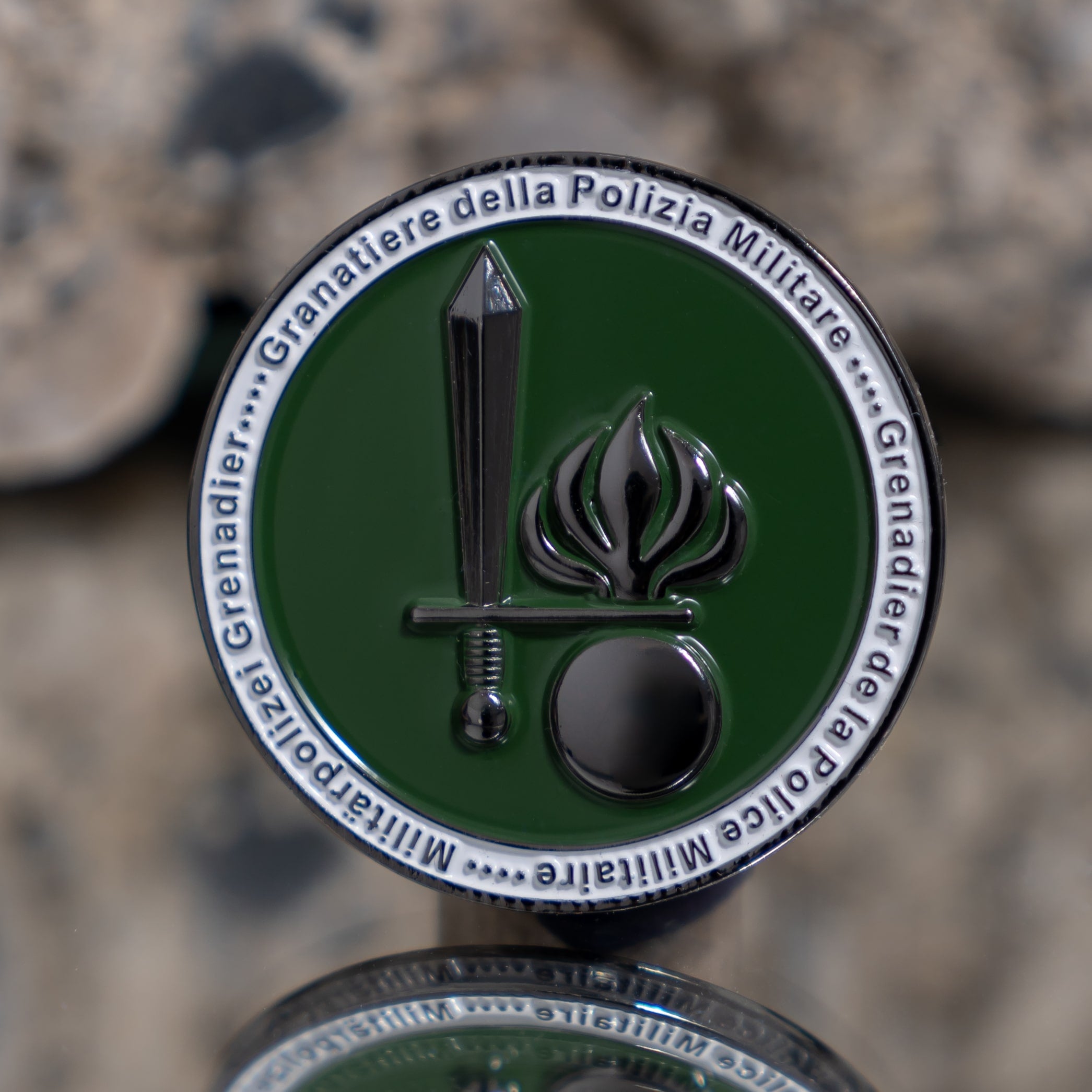 Ein grüner Army Coin Ch mit Schwert- und Flammensymbol auf steinigem Hintergrund.